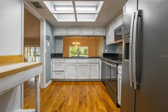 kitchen featuring white cabinets, appliances with stainless steel finishes, decorative light fixtures, an inviting chandelier, and a sink