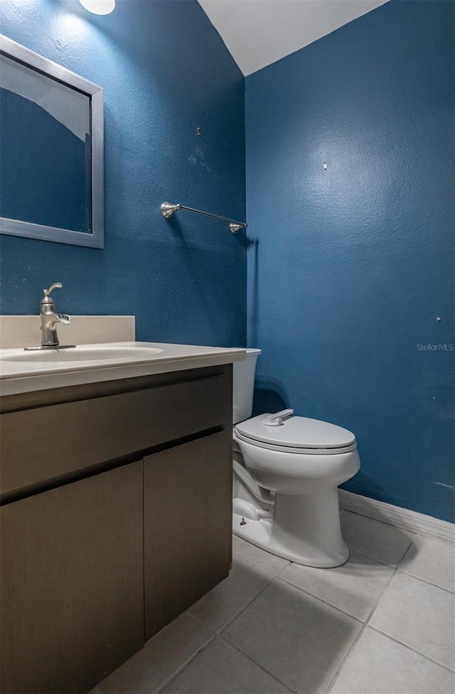 half bathroom with toilet, tile patterned flooring, baseboards, and vanity