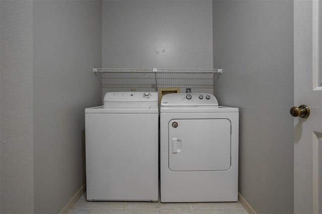 clothes washing area with light tile patterned floors, laundry area, washer and clothes dryer, and baseboards