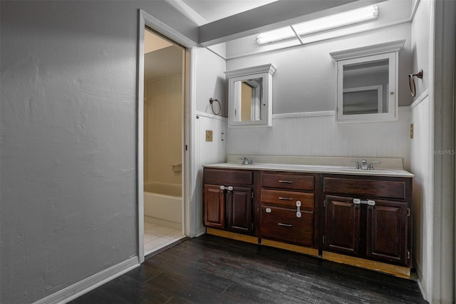 full bathroom featuring a wainscoted wall, double vanity, wood finished floors, and a sink