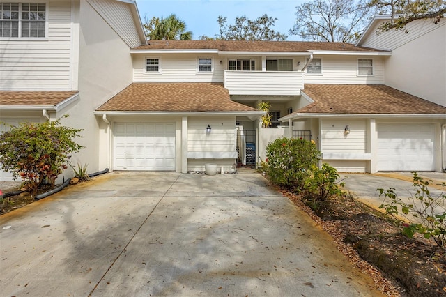 multi unit property with a garage, driveway, a shingled roof, and stucco siding