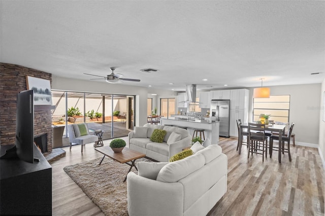 living room with visible vents, ceiling fan, a wood stove, a textured ceiling, and light wood-style floors