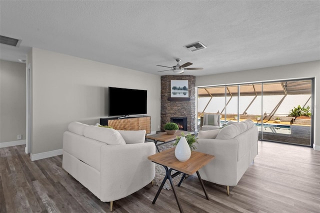 living area featuring a sunroom, visible vents, wood finished floors, and a stone fireplace