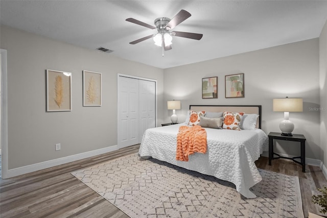 bedroom with baseboards, visible vents, ceiling fan, wood finished floors, and a closet