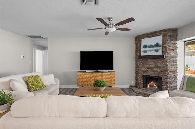 living area featuring a fireplace, visible vents, ceiling fan, a textured ceiling, and wood finished floors