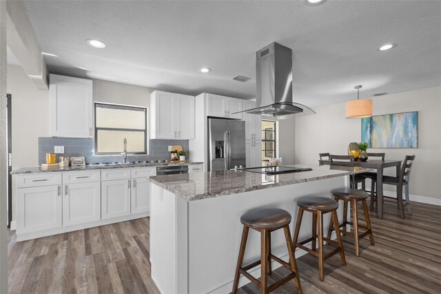 kitchen with a breakfast bar, island exhaust hood, black electric stovetop, a sink, and stainless steel fridge