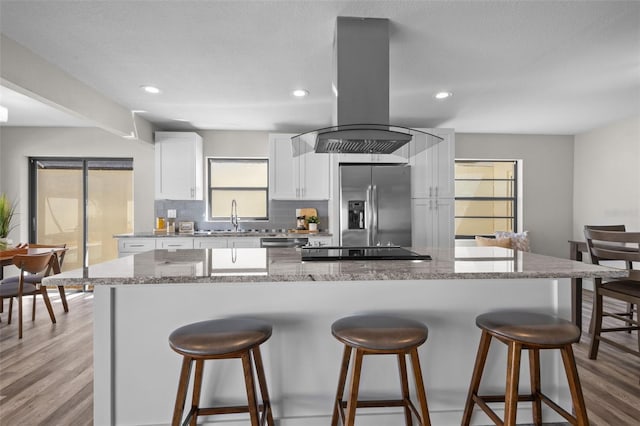 kitchen with island range hood, stainless steel fridge with ice dispenser, a breakfast bar, wood finished floors, and backsplash