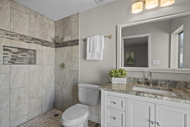 bathroom with toilet, tiled shower, and vanity