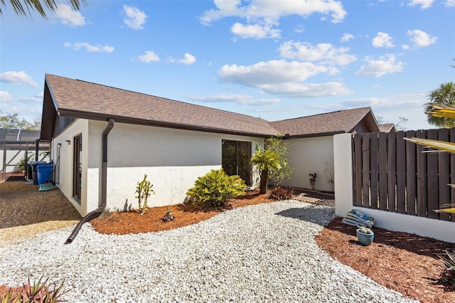 view of property exterior featuring a shingled roof, a lanai, fence, and stucco siding