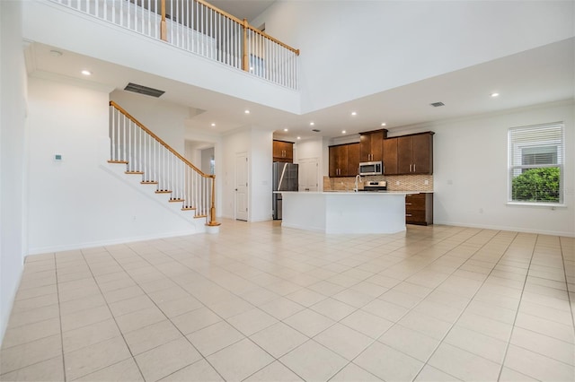 unfurnished living room with light tile patterned floors, baseboards, a towering ceiling, stairs, and crown molding