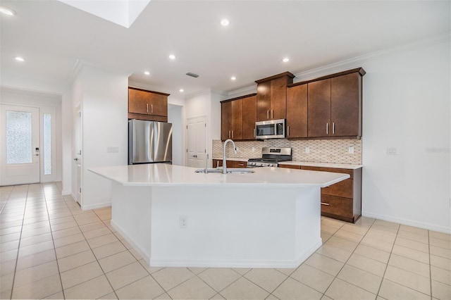 kitchen with decorative backsplash, appliances with stainless steel finishes, a kitchen island with sink, light countertops, and a sink