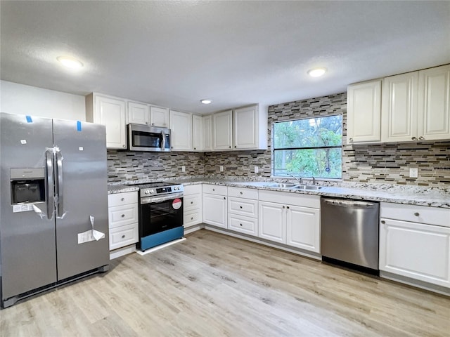 kitchen with light stone countertops, stainless steel appliances, light wood-type flooring, white cabinetry, and a sink