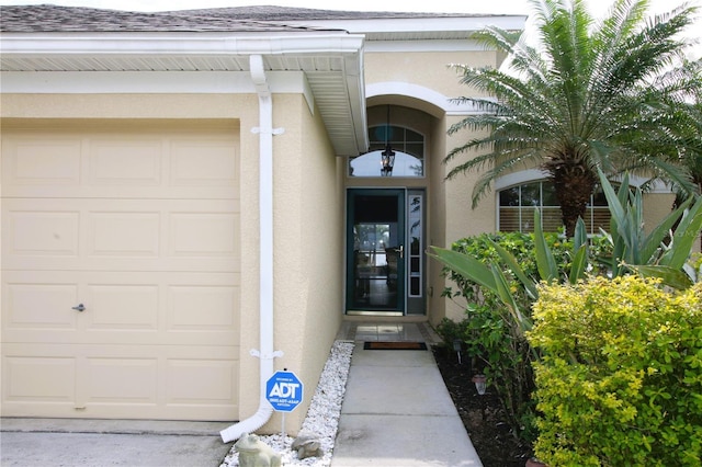 entrance to property with a garage, a shingled roof, and stucco siding