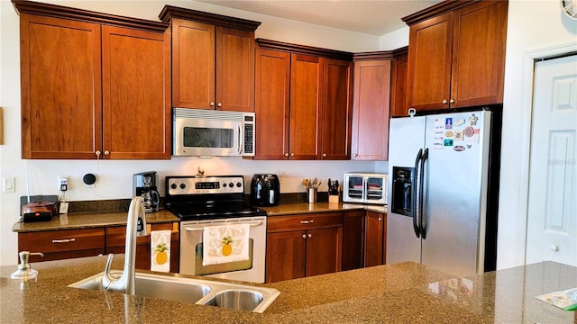 kitchen with appliances with stainless steel finishes, dark stone counters, brown cabinets, and a sink