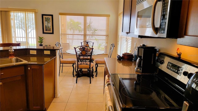 kitchen featuring appliances with stainless steel finishes, dark countertops, light tile patterned flooring, and a sink