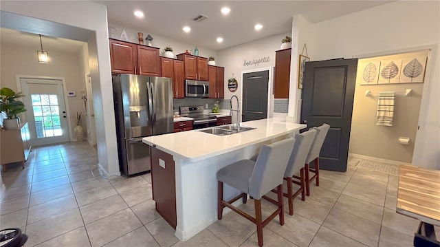 kitchen featuring stainless steel appliances, a sink, light countertops, a kitchen bar, and pendant lighting