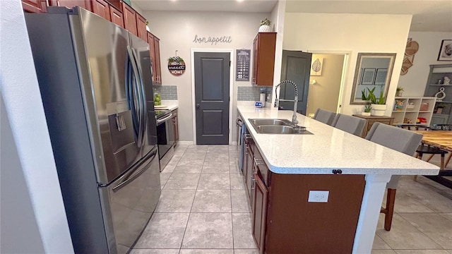 kitchen featuring a breakfast bar, stainless steel appliances, tasteful backsplash, light tile patterned flooring, and a sink