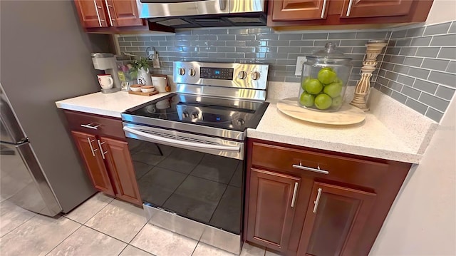 kitchen with reddish brown cabinets, stainless steel appliances, light countertops, backsplash, and light tile patterned flooring