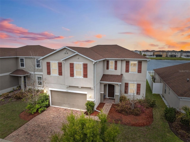 traditional home featuring decorative driveway, stucco siding, a shingled roof, an attached garage, and fence