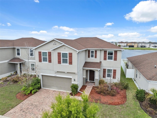 traditional home featuring decorative driveway, stucco siding, an attached garage, fence, and a front lawn