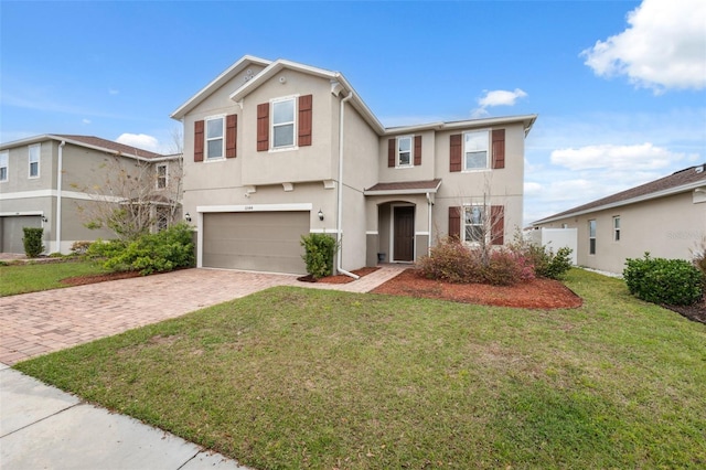 traditional-style home with an attached garage, decorative driveway, a front yard, and stucco siding