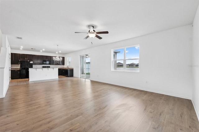 unfurnished living room with ceiling fan with notable chandelier, visible vents, light wood-style flooring, and baseboards