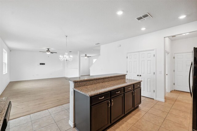 kitchen with light tile patterned floors, ceiling fan with notable chandelier, visible vents, open floor plan, and light stone countertops