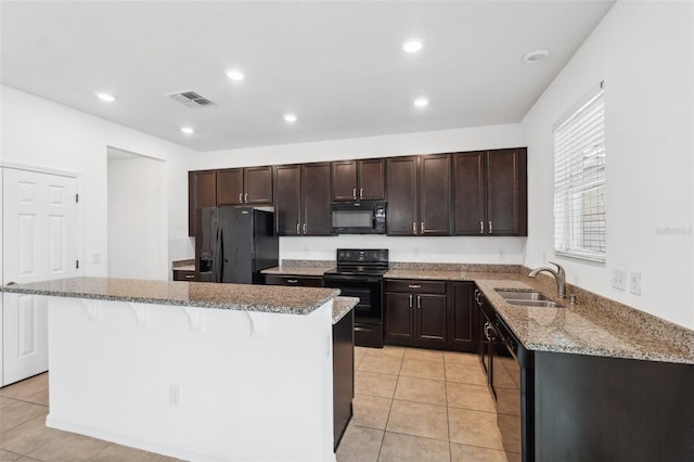 kitchen with light stone counters, a kitchen bar, visible vents, a sink, and black appliances