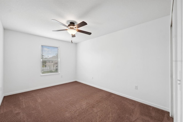 empty room with baseboards, dark carpet, and ceiling fan