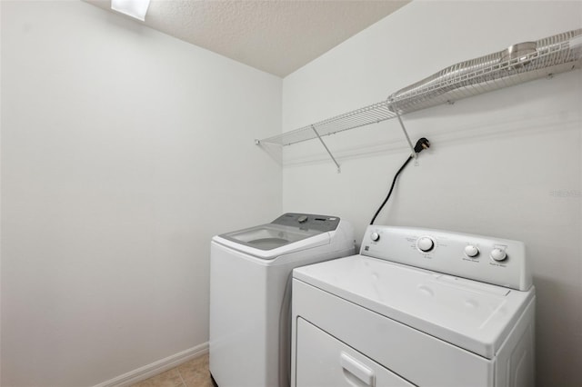 laundry room featuring washing machine and clothes dryer, light tile patterned floors, a textured ceiling, laundry area, and baseboards