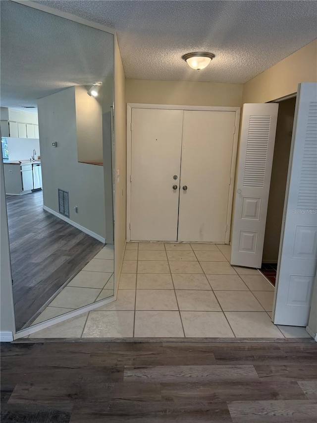 foyer with visible vents, baseboards, a textured ceiling, and light wood finished floors