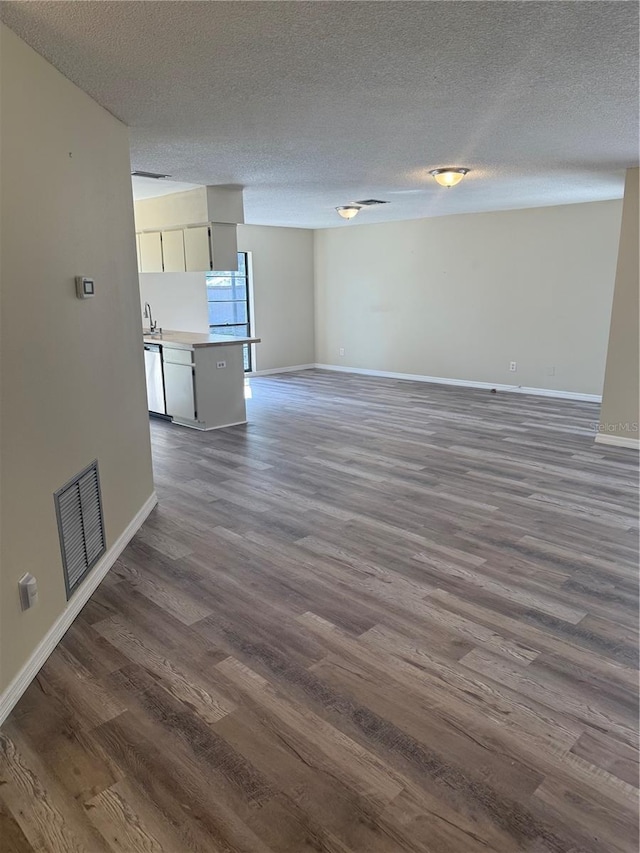 unfurnished living room featuring visible vents, baseboards, a textured ceiling, and dark wood finished floors