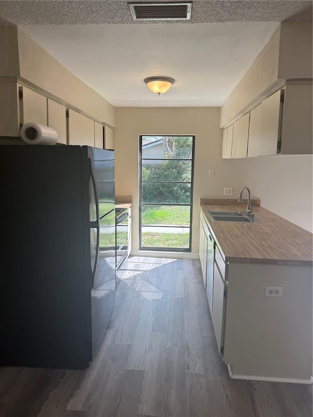 kitchen featuring visible vents, a sink, freestanding refrigerator, white cabinets, and dark wood-style flooring