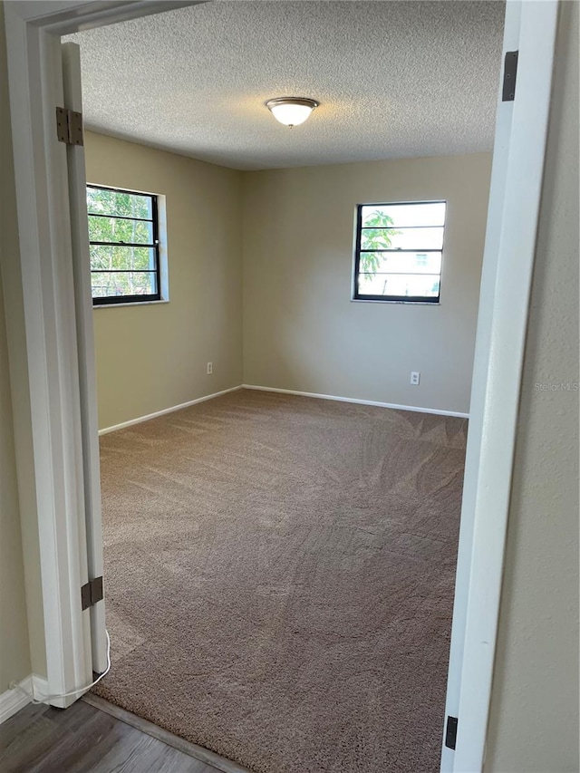 spare room featuring a textured ceiling, baseboards, and dark colored carpet