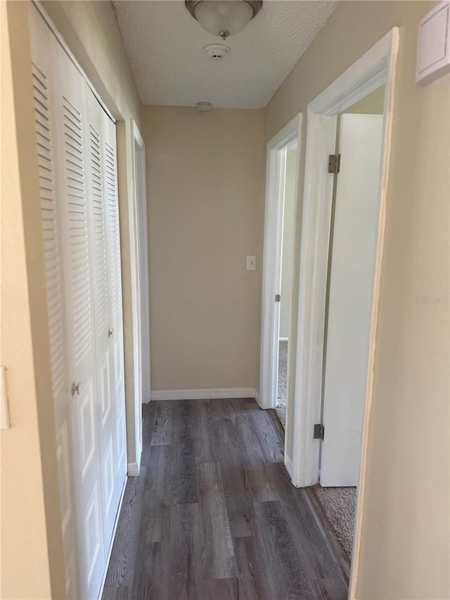 hall featuring baseboards, a textured ceiling, and dark wood-style flooring