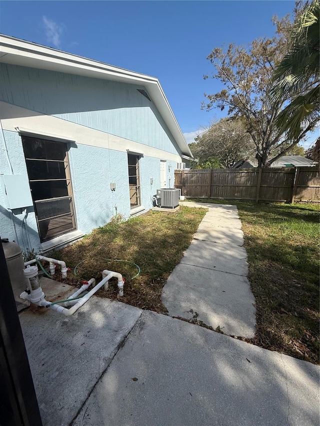 view of side of property featuring a patio, a lawn, central AC unit, and fence