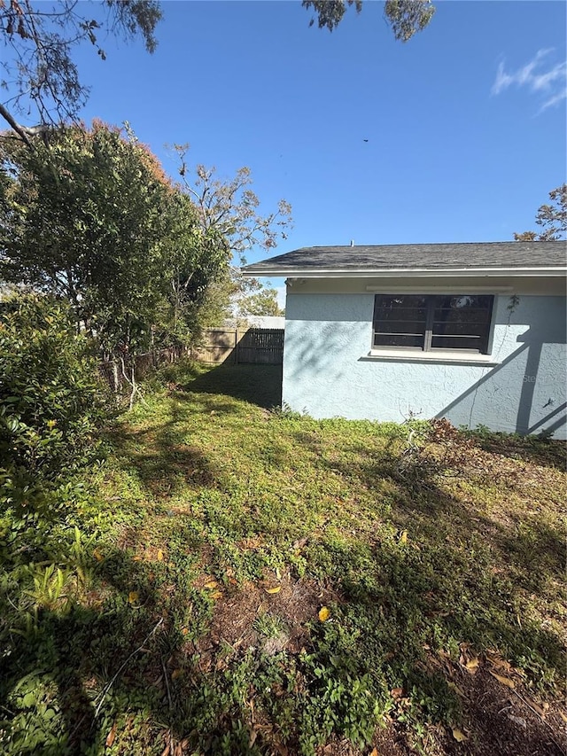 view of side of home featuring a yard, fence, and stucco siding