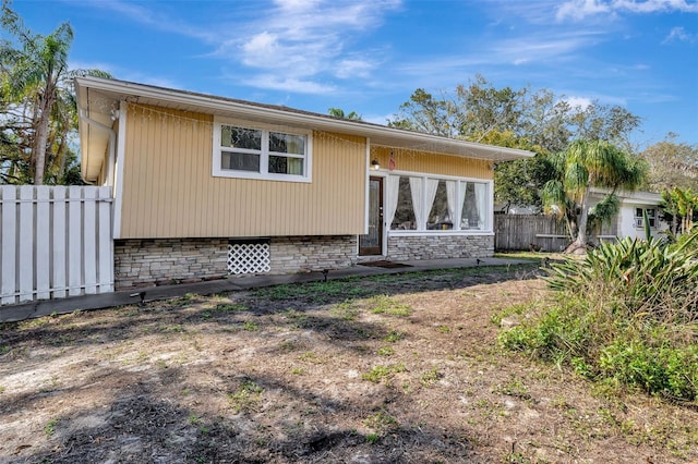 back of property with stone siding, crawl space, and fence