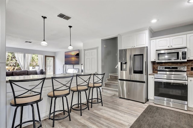 4716 Gazania St, New Port Richey, FL 34652 - kitchen with light wood finished floors, stainless steel appliances, visible vents, white cabinets, and a kitchen bar