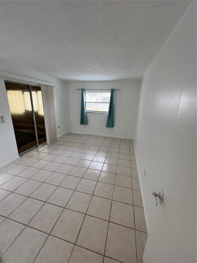 spare room with light tile patterned floors, baseboards, and a textured ceiling