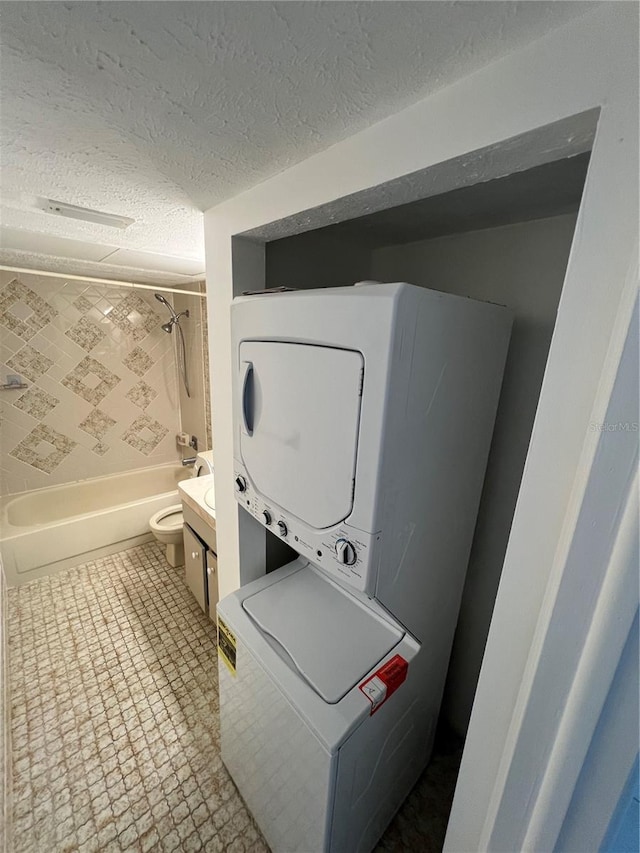 laundry room with a textured ceiling, laundry area, stacked washing maching and dryer, and tile patterned flooring