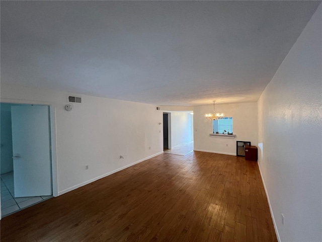 unfurnished living room featuring baseboards, visible vents, a chandelier, and wood finished floors