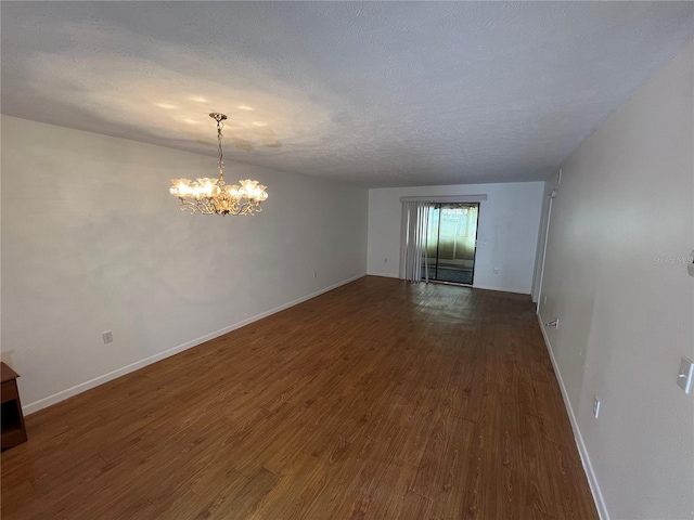 empty room with a textured ceiling, baseboards, dark wood finished floors, and a notable chandelier