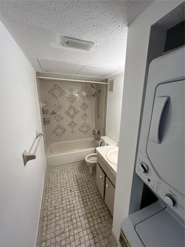 full bath with stacked washer and dryer, toilet, washtub / shower combination, vanity, and a textured ceiling