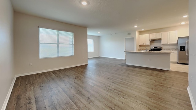 kitchen with appliances with stainless steel finishes, light wood-style floors, open floor plan, white cabinetry, and light stone countertops