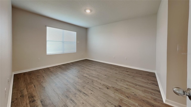 unfurnished room featuring a textured ceiling, baseboards, and wood finished floors