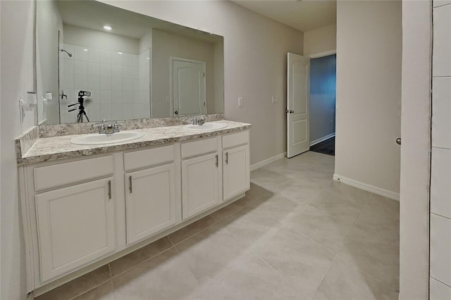 full bathroom featuring double vanity, walk in shower, a sink, and baseboards