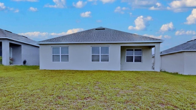 back of property with a yard, roof with shingles, and stucco siding