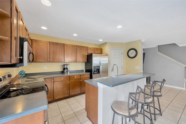 kitchen with light tile patterned floors, appliances with stainless steel finishes, a breakfast bar, a kitchen island with sink, and recessed lighting