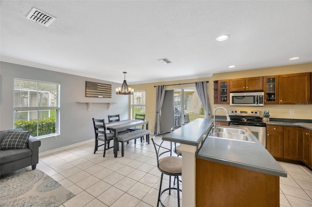 kitchen featuring light tile patterned floors, visible vents, appliances with stainless steel finishes, brown cabinets, and a sink